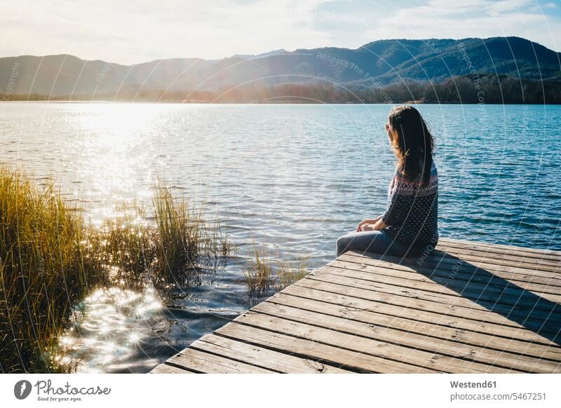 Frau sitzt bei Sonnenuntergang auf einer Holzplattform an einem See Seen erholen erholend sitzen sitzend weiblich Frauen Steg Stege Anlegestelle Gewässer Wasser