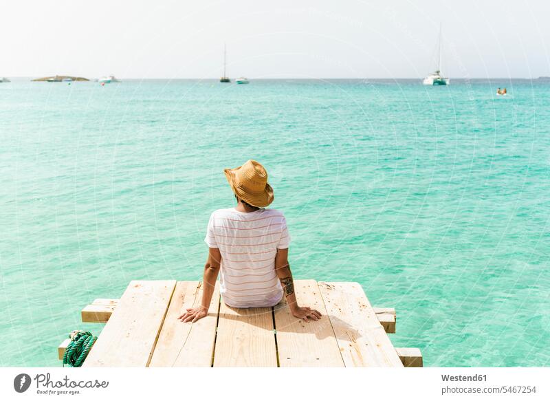 Rückenansicht eines auf einem Holzsteg sitzenden Mannes mit Blick aufs Meer, Formentera, Spanien Leute Menschen People Person Personen Europäisch Kaukasier