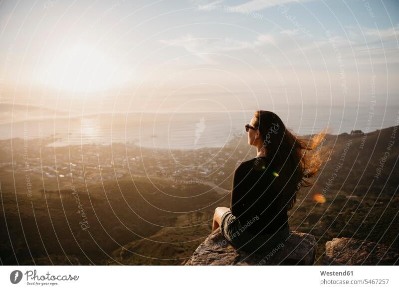 Südafrika, Kapstadt, Kloof Nek, Frau sitzt auf Felsen bei Sonnenuntergang weiblich Frauen sitzen sitzend Sonnenuntergänge Erwachsener erwachsen Mensch Menschen
