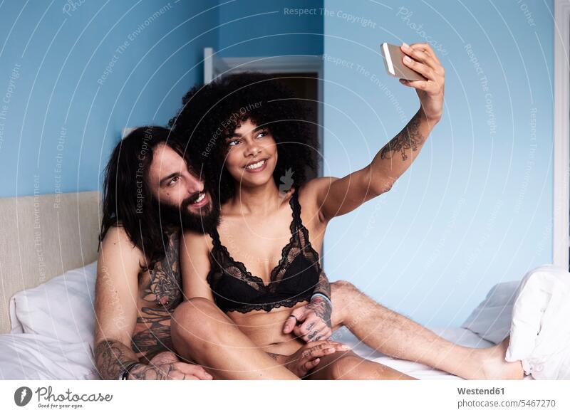 Glückliches, zärtliches, junges Paar, das ein Selfie im Bett macht Pärchen Paare Partnerschaft Selfies glücklich glücklich sein glücklichsein Betten Zuneigung
