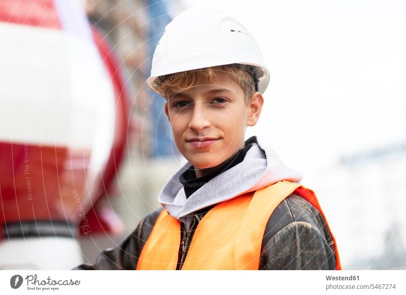 Selbstbewusster männlicher Teenager, der auf der Baustelle einen Schutzhelm und reflektierende Kleidung trägt Farbaufnahme Farbe Farbfoto Farbphoto Deutschland