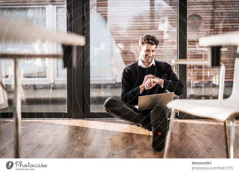 Geschäftsmann sitzt auf dem Boden seines Büros, mit Laptop und Smartwatch sitzen sitzend auf dem Boden sitzen auf dem Boden sitzend benutzen benützen