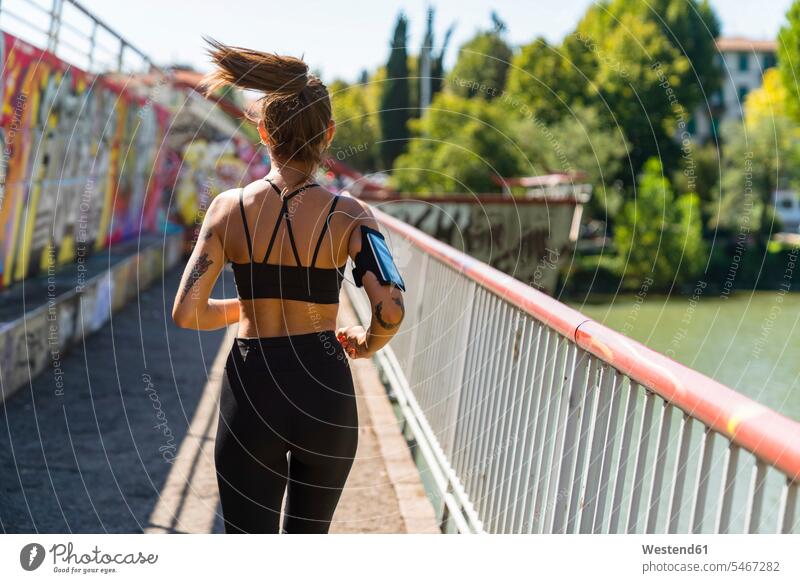 Rückansicht einer jungen Frau, die auf einer Brücke läuft Telekommunikation telefonieren Handies Handys Mobiltelefon Mobiltelefone hoeren rennen Jahreszeiten