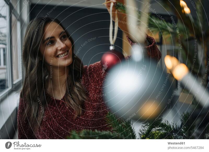 Lächelnde junge Frau schmückt Weihnachtsbaum Europäer Kaukasier Europäisch kaukasisch Freude freuen lächeln Tradition Brauchtum traditionell Christbaumkugel