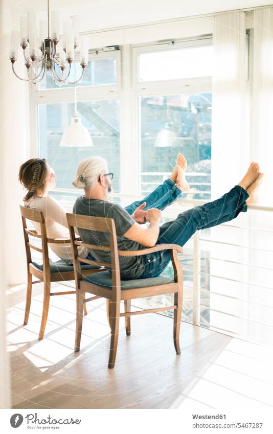 Entspanntes reifes Paar, das zu Hause auf Stühlen mit erhobenen Füßen sitzt Zuhause daheim Stuhl Stuehle entspannt entspanntheit relaxt sitzen sitzend Pärchen