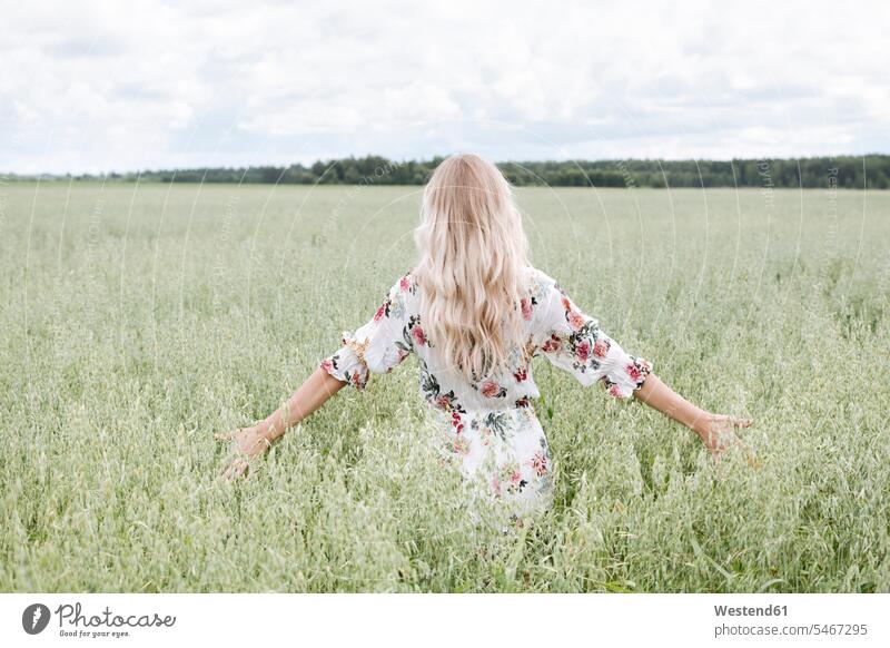 Junge Frau mit blonden Haaren steht inmitten eines Haferfeldes vor bewölktem Himmel Farbaufnahme Farbe Farbfoto Farbphoto Freizeitbeschäftigung Muße Zeit