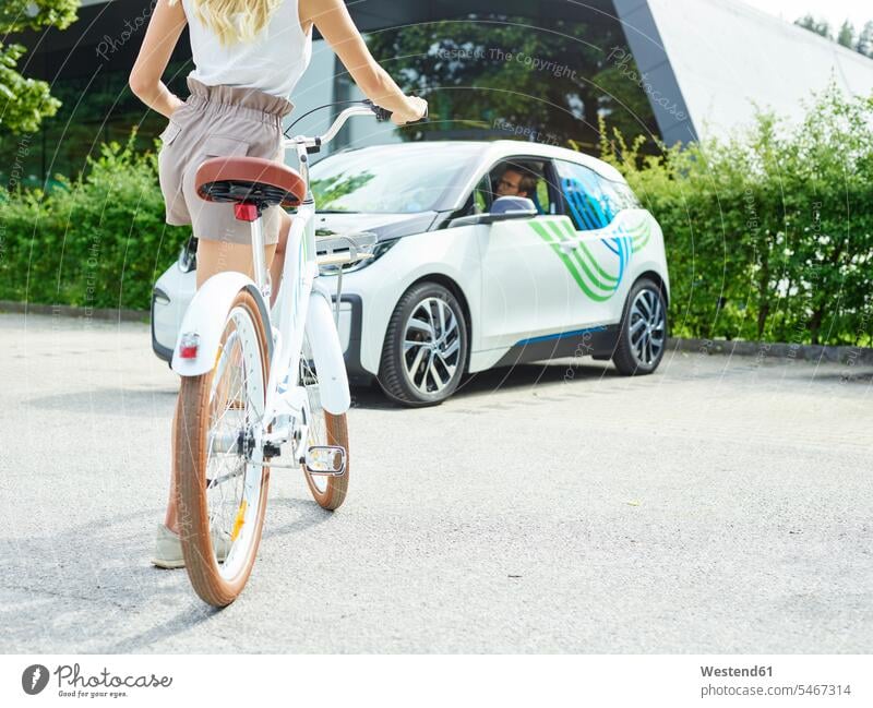 Frau mit Fahrrad vor Elektroauto Elektromobil Elektromobile Elektroautos Auto Wagen PKWs Automobil Autos Bikes Fahrräder Räder Rad Elektrofahrzeug