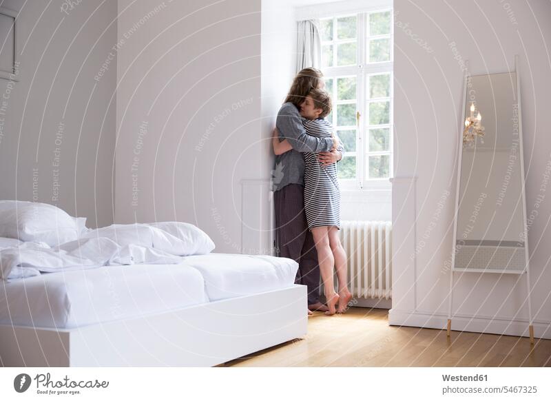 Junges Paar umarmt sich zu Hause am Fenster im Schlafzimmer Betten Arm umlegen Umarmung Umarmungen freuen behüten behütet geborgen Sicherheit Glück