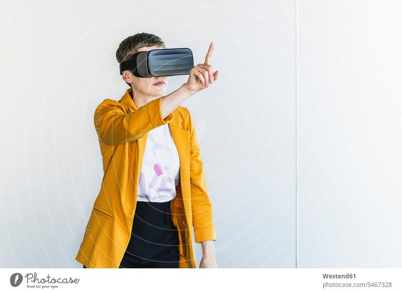 Geschäftsfrau im Blazer, die durch einen Virtual-Reality-Simulator schaut, während sie im Büro an der Wand steht Farbaufnahme Farbe Farbfoto Farbphoto
