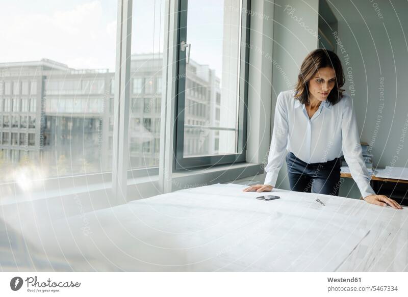 Geschäftsfrau bei der Arbeit im Büro, schaut auf Blaupausen Architektin Architektinnen Bauplan Architekturplan Konstruktionsplan Konstruktionszeichnung