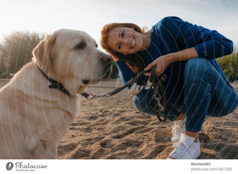 Deutschland, Hamburg, lächelnde Frau mit Hund am Strand am Elbufer glücklich Glück glücklich sein glücklichsein Flussufer Hunde weiblich Frauen Ufer Haustier