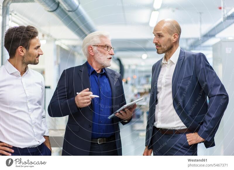 Leitender männlicher Manager diskutiert mit Kollegen über ein digitales Tablet, während er in einer beleuchteten Fabrik steht Farbaufnahme Farbe Farbfoto