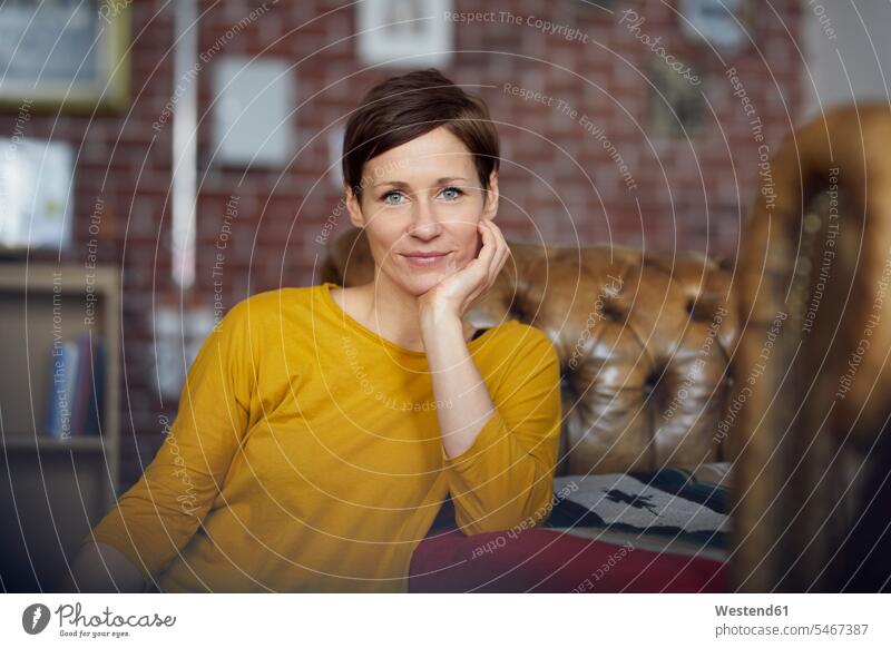 Attraktive Frau sitzt zu Hause mit der Hand am Kinn T-Shirt T-Shirts nachdenken überlegen Portrait Porträts Portraits attraktiv schoen gut aussehend schön