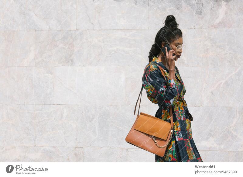 Porträt einer schicken Frau im gemusterten Kleid, die mit einem Handy telefoniert Kleider Telekommunikation telefonieren Handies Handys Mobiltelefon