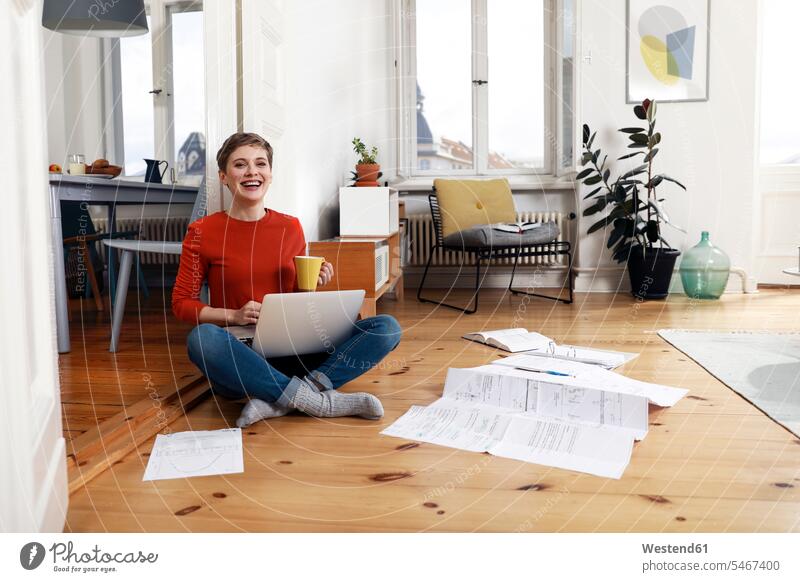 Frau sitzt im Schneidersitz auf dem Boden ihres Hauses und benutzt einen Laptop Dokument Dokumente Papiere Unterlagen Aktenordner Mappe Ordner sitzen sitzend