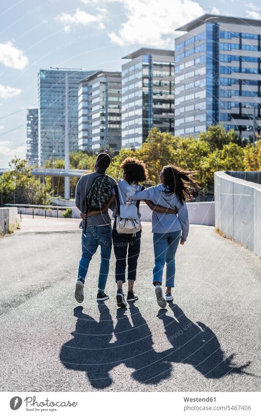 Drei Freunde erkunden die Stadt, gehen die Straße entlang, Arm in Arm gehend geht Urban städtisch Urbanität Urbanitaet Erforschung Erkundung erforschen