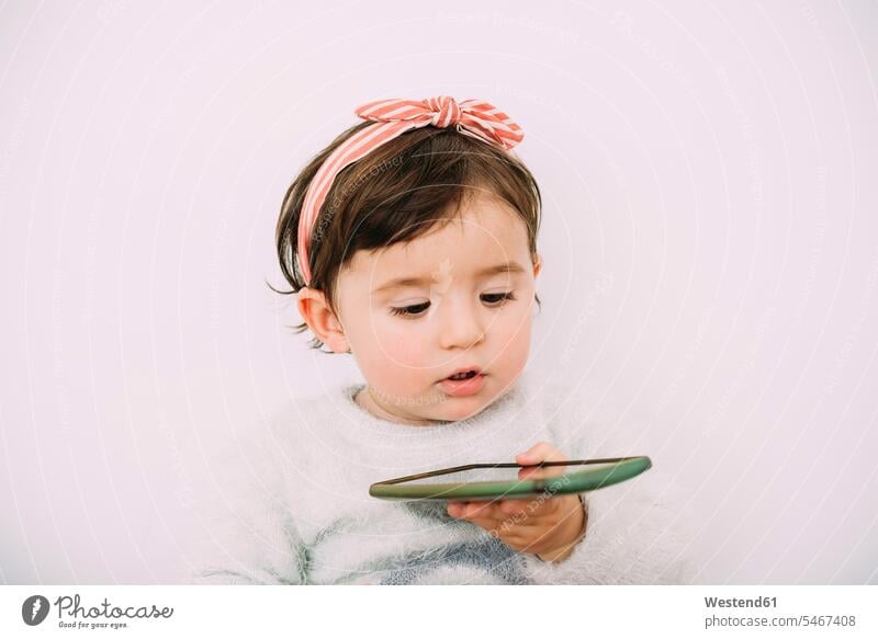 Porträt eines kleinen Mädchens, das auf ein Handy schaut Smartphone iPhone Smartphones Portrait Porträts Portraits ansehen weibliche Babys weibliches Baby