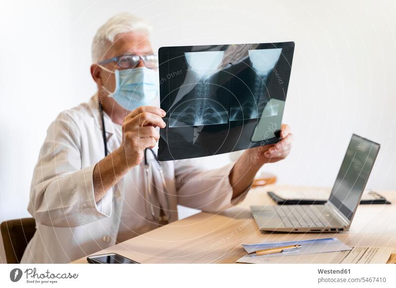 Arzt untersucht medizinisches Röntgenbild des menschlichen Halses während er in der Klinik sitzt Farbaufnahme Farbe Farbfoto Farbphoto Innenaufnahme