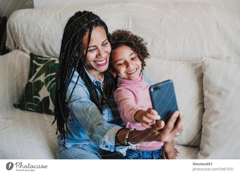 Porträt einer glücklichen Mutter und ihrer kleinen Tochter, die ein Selfie mit ihrem Smartphone auf der Couch machen Couches Liege Sofas Handies Handys