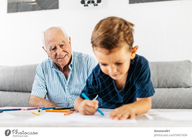 Porträt eines lächelnden Großvaters, der seinen Enkel beim Zeichnen mit Buntstiften beobachtet Enkelsöhne Enkelsohn Portrait Porträts Portraits Opa Großpapa
