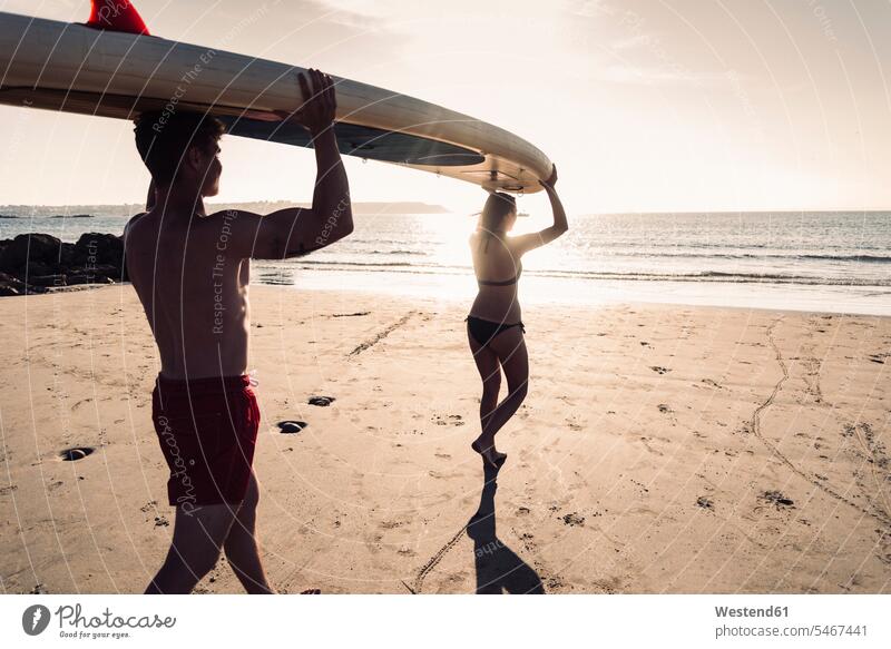 Frankreich, Bretagne, junges Paar mit einem SUP-Board am Strand zusammen Pärchen Paare Partnerschaft Beach Straende Strände Beaches tragen transportieren