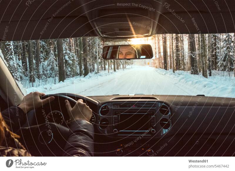 Finnland, Kuopio, Frau fährt Auto in Winterlandschaft bei Sonnenuntergang Autoreise Fahrzeuginnenraum Reisende Reisender Linsenreflexion Blendenflecken