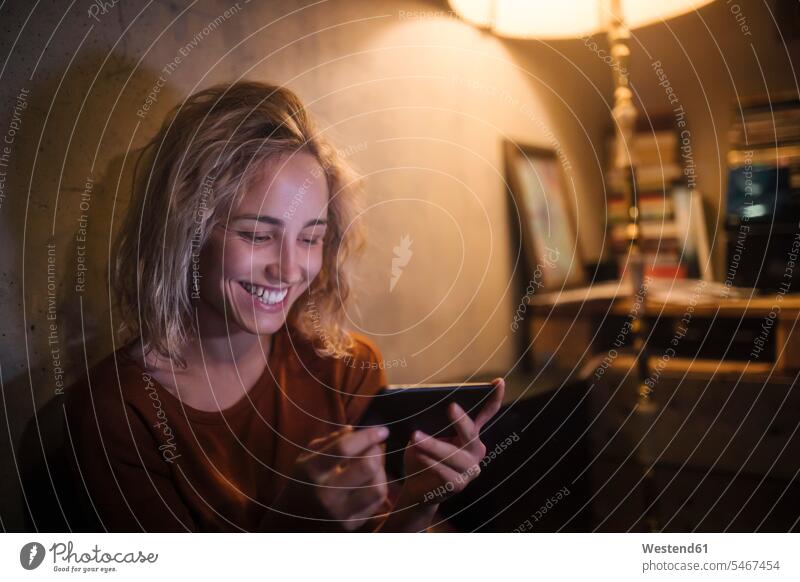 Porträt einer lachenden jungen Frau, die zu Hause ein Smartphone benutzt Handy Film wohnen Abend Freude Zuhause lustig Stimmung Beleuchtung Einfachheit Freizeit
