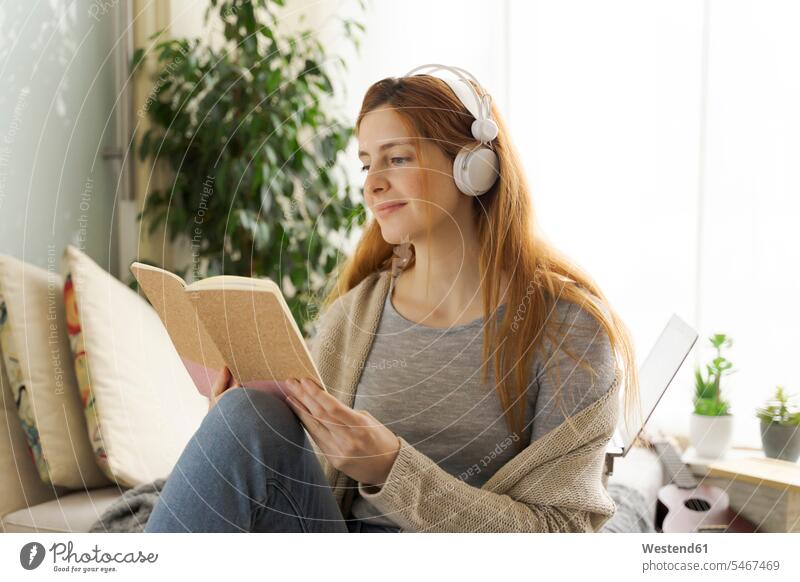 Junge Frau mit Kopfhörern und Leseheft zu Hause Leute Menschen People Person Personen Europäisch Kaukasier kaukasisch 1 Ein ein Mensch eine nur eine Person