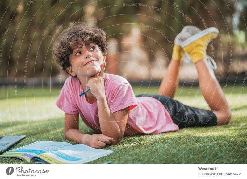 Junge liegt im Garten und macht Hausaufgaben Ausbildung Schueler Schulkinder Schüler Leute Menschen People Person Personen gelockt gelockte Haare gelocktes Haar