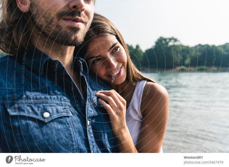 Lächelnde junge Frau, die sich am Flussufer an die Schulter eines Mannes lehnt Paar Pärchen Paare Partnerschaft anlehnen angelehnt lehnend Fluesse Fluß Flüsse