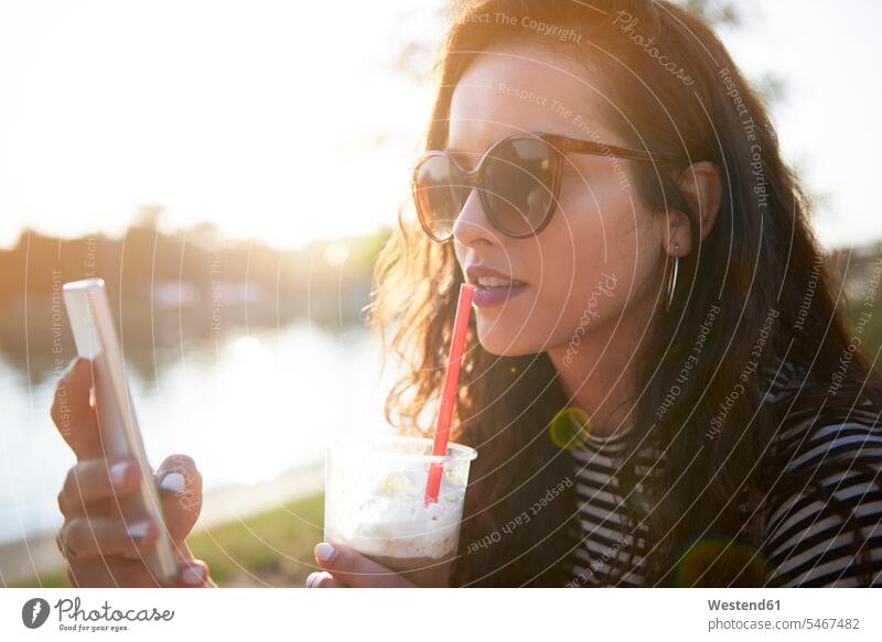 Stilvolle junge Frau mit Handy und Getränk zum Mitnehmen bei Sonnenuntergang im Freien Getraenk Getränke Getraenke Mobiltelefon Handies Handys Mobiltelefone