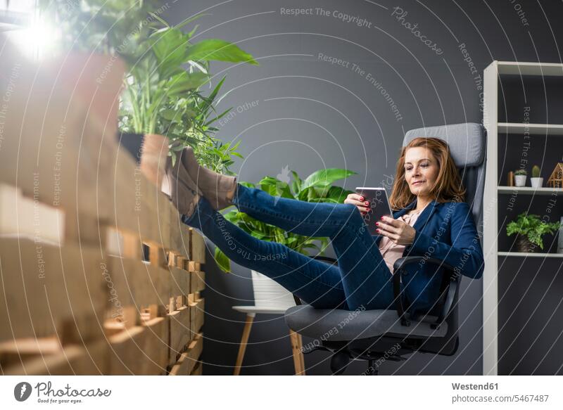 Reife Geschäftsfrau, die in einem nachhaltigen Büro arbeitet und ein digitales Tablet benutzt Grünpflanze Grünpflanzen Gruenpflanze Gruenpflanzen Fensterbank