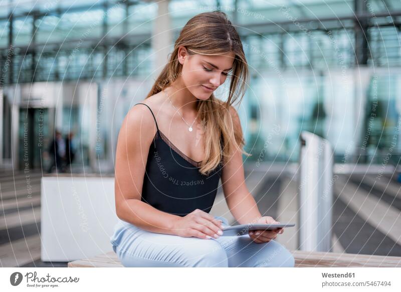 Lächelnde junge Frau sitzt im Freien und benutzt Tablette sitzen sitzend Tablet Computer Tablet-PC Tablet PC iPad Tablet-Computer lächeln weiblich Frauen