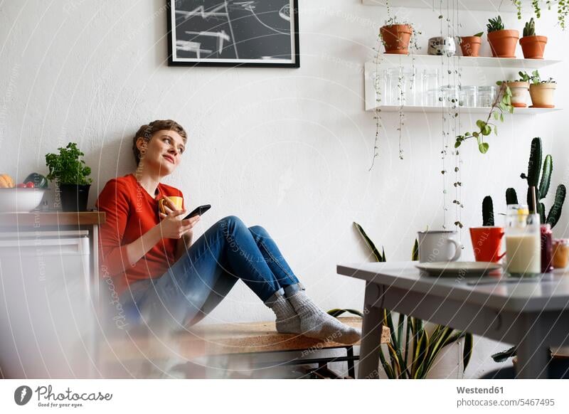 Frau sitzt in der Küche, trinkt Kaffee und hört Smartphone-Nachrichten ab Küchen glücklich Glück glücklich sein glücklichsein sitzen sitzend SMS Textnachricht