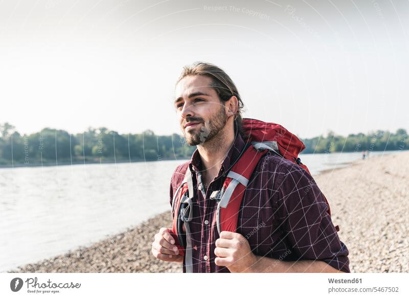 Selbstbewusster junger Mann mit Rucksack am Flussufer Rucksäcke Männer männlich Fluesse Fluß Flüsse Zuversicht Zuversichtlich Selbstvertrauen selbstbewusst