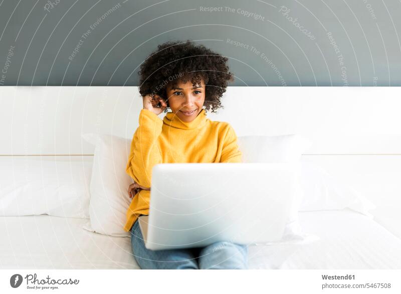 Lächelnde Frau sitzt auf dem Bett und benutzt einen Laptop Notebook Laptops Notebooks weiblich Frauen lächeln Betten sitzen sitzend Computer Rechner Erwachsener