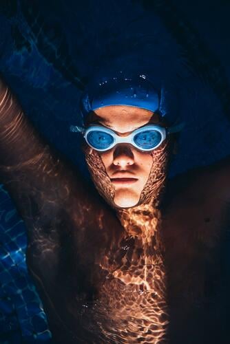 Porträt eines jungen paralympischen Schwimmers, der in einem Schwimmbecken auf dem Wasser schwimmt Farben Farbtoene Farbton Farbtöne blaue blauer blaues