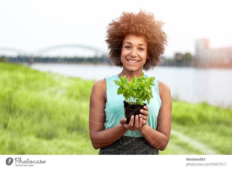 Porträt einer lächelnden Frau, die eine Pflanze im Freien hält weiblich Frauen Pflanzenwelt Flora halten Portrait Porträts Portraits Erwachsener erwachsen