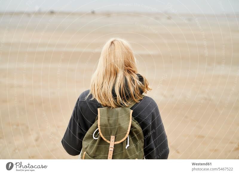 Rückenansicht einer blonden jungen Frau mit Rucksack am Strand weiblich Frauen Beach Straende Strände Beaches blonde Haare blondes Haar Erwachsener erwachsen