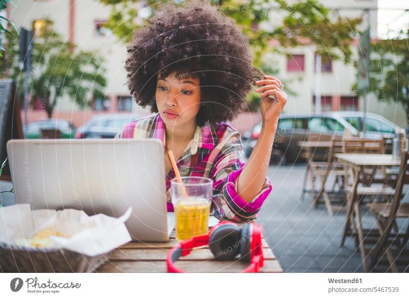 Junge Frau mit Afrofrisur mit Laptop in einem Straßencafé in der Stadt Leute Menschen People Person Personen gelockt gelockte Haare gelocktes Haar lockig