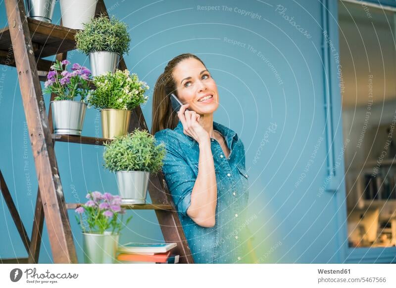 Schöne Frau in ihrer Wohnung, mit Pflanzen geschmückt, telefoniert weiblich Frauen Zuhause zu Hause daheim Smartphone iPhone Smartphones telefonieren anrufen