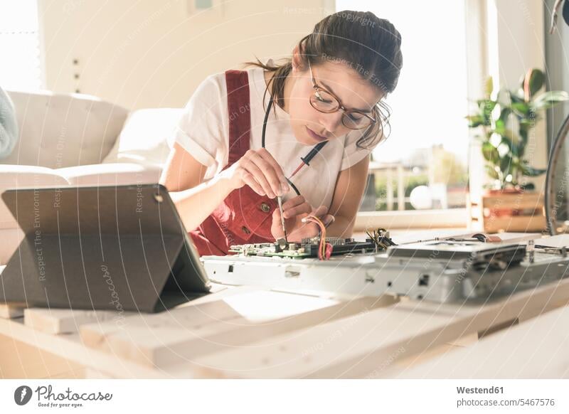 Junge Frau arbeitet an Computerausrüstung zu Hause neben Tablet Deutschland Schaltplatte Leiterplatine Printplatte Kompetenz Fähigkeit Können Wohnen