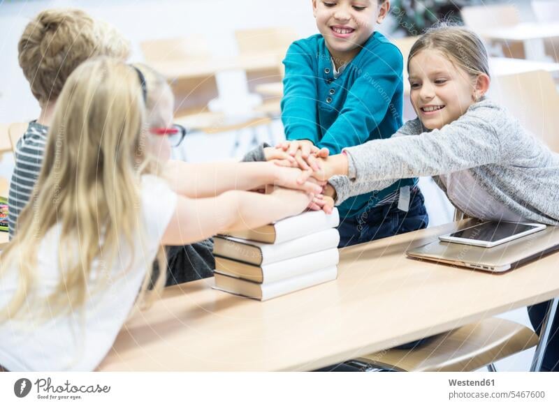 Glückliche Schülerinnen und Schüler, die in der Klasse die Hände auf Bücher stapeln glücklich glücklich sein glücklichsein Schule Schulen Hand Klassenzimmer