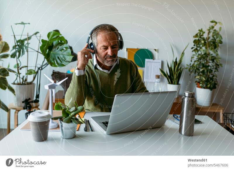 Mann trägt Kopfhörer mit Laptop, während er zu Hause am Tisch sitzt Farbaufnahme Farbe Farbfoto Farbphoto Innenaufnahme Innenaufnahmen innen drinnen Tag