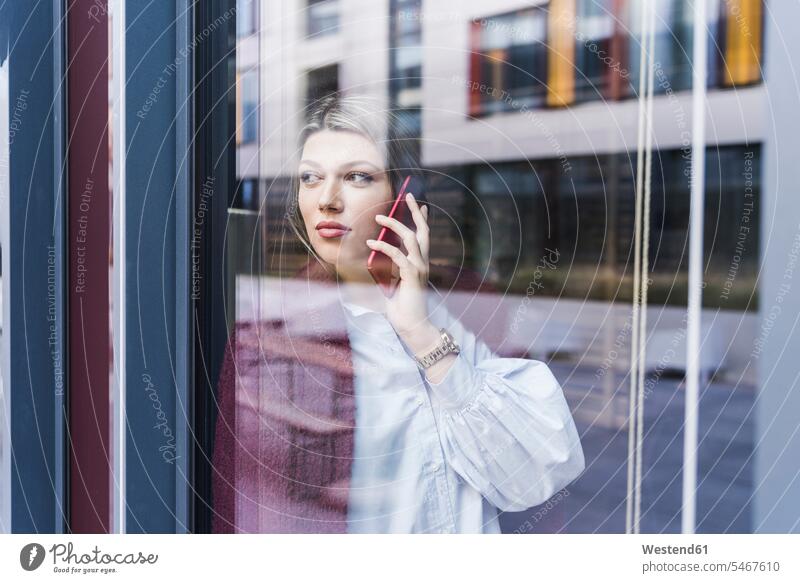 Junge Frau am Handy hinter der Fensterscheibe Fensterscheiben Mobiltelefon Handies Handys Mobiltelefone telefonieren anrufen Anruf telephonieren weiblich Frauen