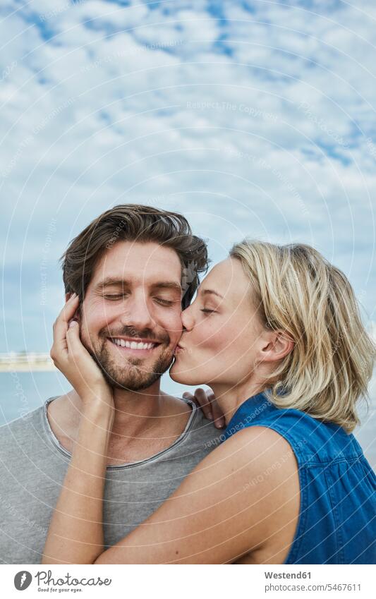 Glückliches junges Paar, das sich am Strand küsst glücklich glücklich sein glücklichsein küssen Küsse Kuss knuddeln umarmen Beach Straende Strände Beaches