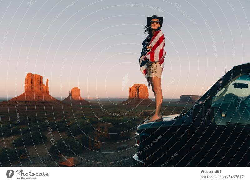 USA, Utah, Monument Valley, Frau mit Flagge der Vereinigten Staaten von Amerika genießt den Sonnenuntergang im Monument Valley stehen stehend steht Fahnen