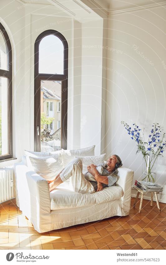 Nachdenkliche Frau, die im Wohnzimmer auf dem Sofa Musik hört Deutschland Innenaufnahme Innenaufnahmen innen drinnen Tag Tageslichtaufnahme Tageslichtaufnahmen