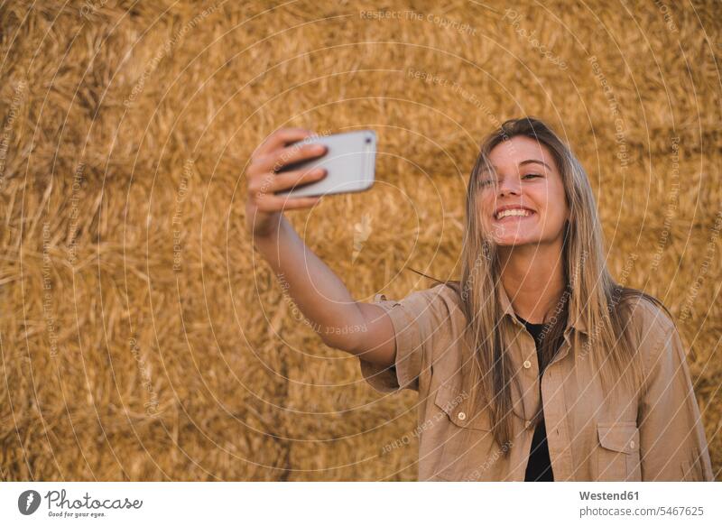 Junge Frau steht vor Heuballen und macht ein Smartphone-Selfie weiblich Frauen schön Erwachsener erwachsen Mensch Menschen Leute People Personen Gras Gräser