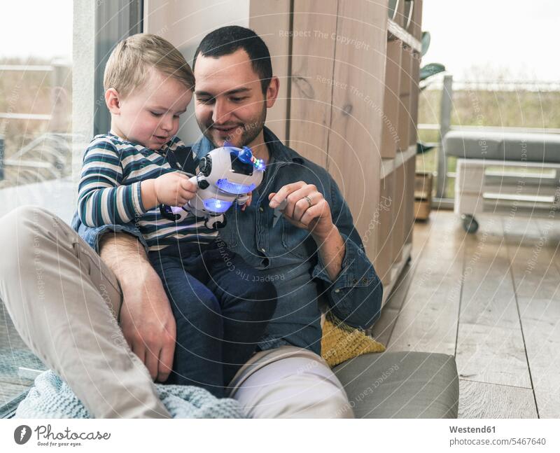 Vater und Sohn spielen mit einem Spielzeugroboter zu Hause Zuhause daheim Papas Väter Vati Vatis Papis Söhne Roboter Eltern Familie Familien Mensch Menschen